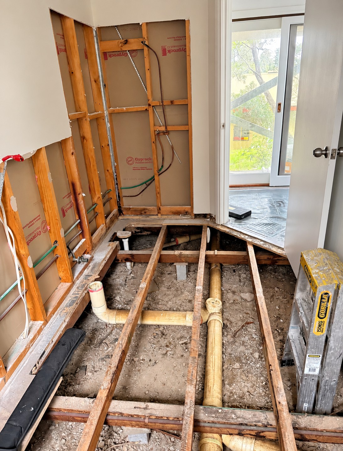 Bathroom during demolition: exposed timber framing, plumbing and the stripped-back floor